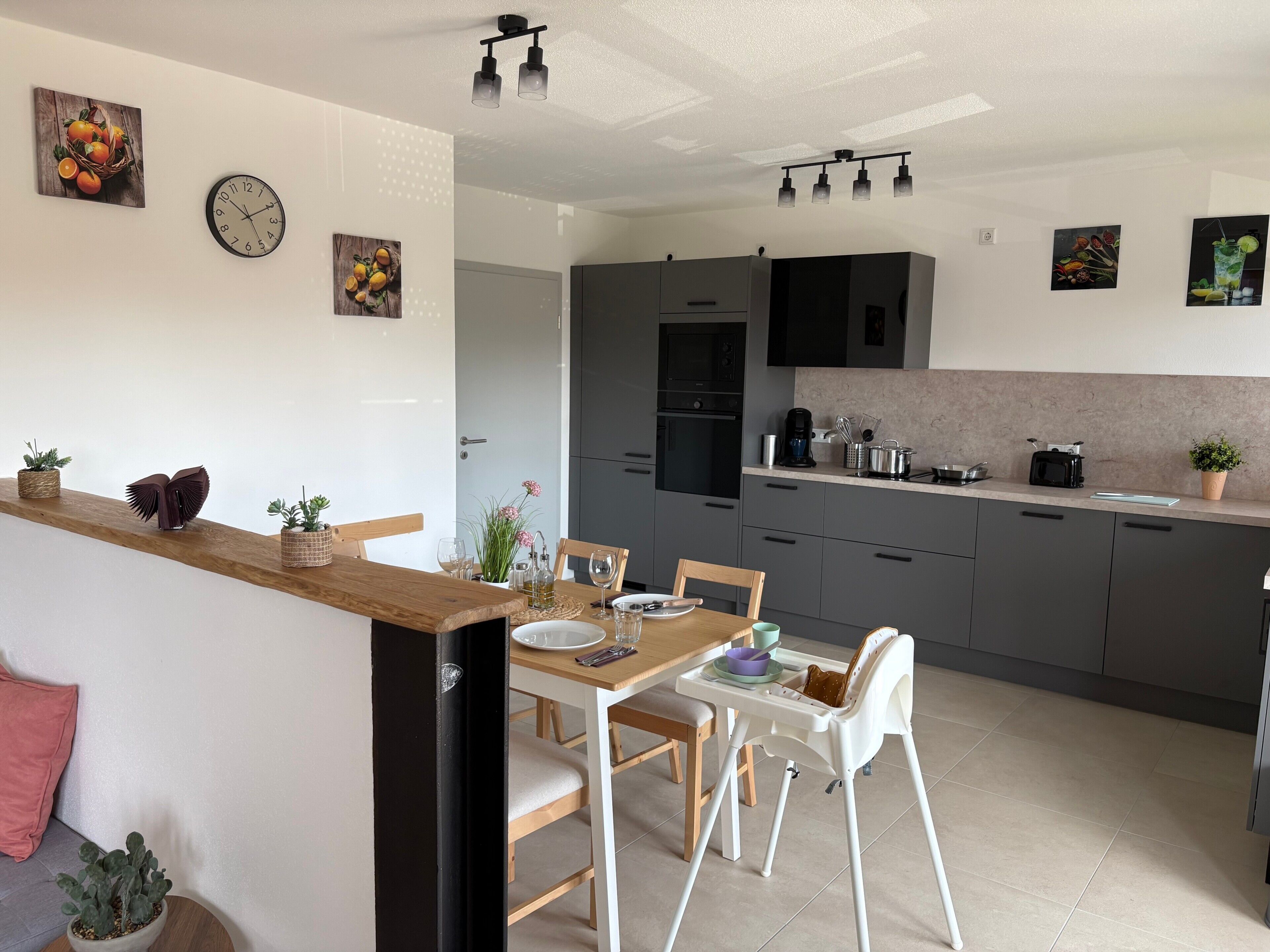 Una cocina moderna con armarios grises, encimera de madera y una zona de comedor con mesa y sillas blancas.