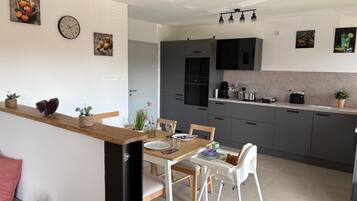 Una cocina moderna con armarios grises, encimera de madera y una zona de comedor con mesa y sillas blancas.