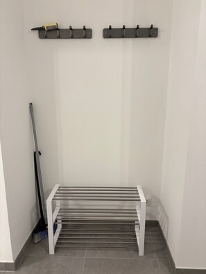A room with a white bench, a broom, and two wall-mounted hooks.