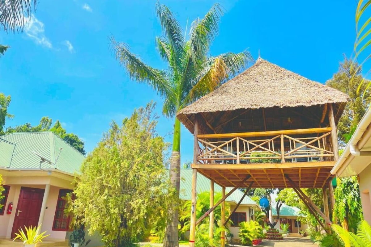 A bungalow with a thatched roof, surrounded by lush greenery and palm trees.