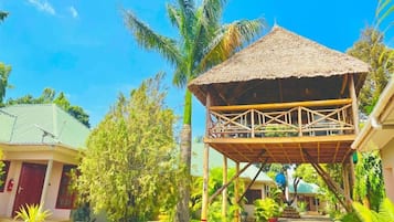 A bungalow with a thatched roof, surrounded by lush greenery and palm trees.