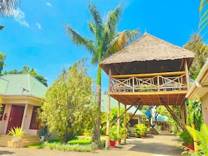 A bungalow with a thatched roof, surrounded by lush greenery and palm trees. - Kili Palladium Homes Apartments - Soweto (Moshi)