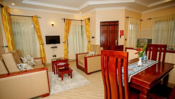 A living room with a sofa, a coffee table, and a dining table with chairs. - Kili Palladium Homes Apartments - Soweto (Moshi)