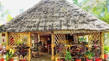A thatched-roof structure with a covered seating area and potted plants.