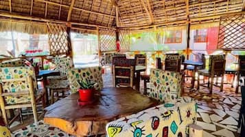 A restaurant with thatched roof, colorful patterned furniture, and a tiled floor.