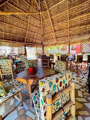 A restaurant with thatched roof, colorful patterned furniture, and a tiled floor. - Kili Palladium Homes Apartments - Soweto (Moshi)