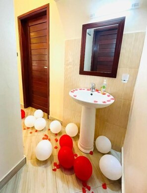 Un baño con lavamanos pedestal, puerta de madera y espejo.