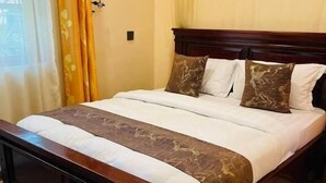 A bed with a wooden frame, a white mattress, and a brown decorative cover. - Kili Palladium Homes Apartments - Soweto (Moshi)