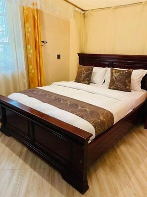 A bed with a wooden frame, a white mattress, and a brown decorative cover. - Kili Palladium Homes Apartments - Soweto (Moshi)