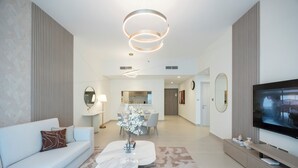 A modern living room with a sofa, coffee table, TV, and a dining area in the background. - Bloomfields 1BR in Fairways 1 - Yas (Abu Dhabi)