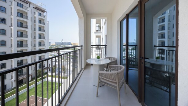A balcony with a table and chairs, overlooking a cityscape with high-rise buildings. - Bloomfields 1BR in Fairways 1 - Yas (Abu Dhabi)
