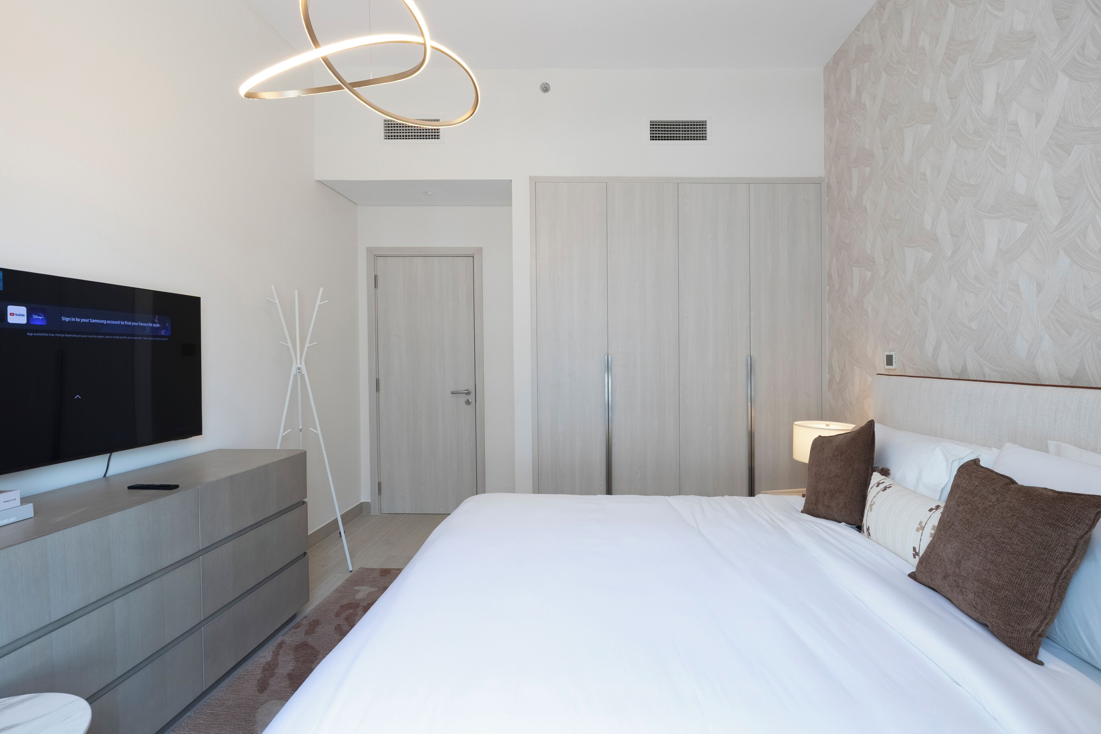 A modern hotel room with a bed, a television, a desk, and a wardrobe.
