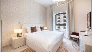 A modern hotel room with a large bed, bedside tables, a desk, and a view of a building through the window. - Bloomfields 1BR in Fairways 1 - Yas (Abu Dhabi)