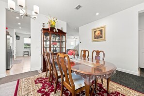 A dining room with a wooden table, chairs, a chandelier, a vase with flowers, a cabinet, and a framed picture on the wall. - 5BR w/ Pool Table & Fire pit near Madeira Beach (Pinellas Park)
