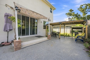Ein überdachter Patio-Bereich mit Tisch und Stühlen, eine Pergola und ein überdachter Sitzbereich mit Liegestühlen.