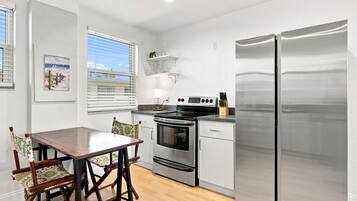 A compact kitchen with a stainless steel refrigerator, an oven, and a stove. There is a wooden dining table with chairs.