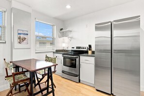 A compact kitchen with a stainless steel refrigerator, an oven, and a stove. There is a wooden dining table with chairs. - 2BR Beachview & Heated Pool | Direct Beach Access (St. Pete Beach)