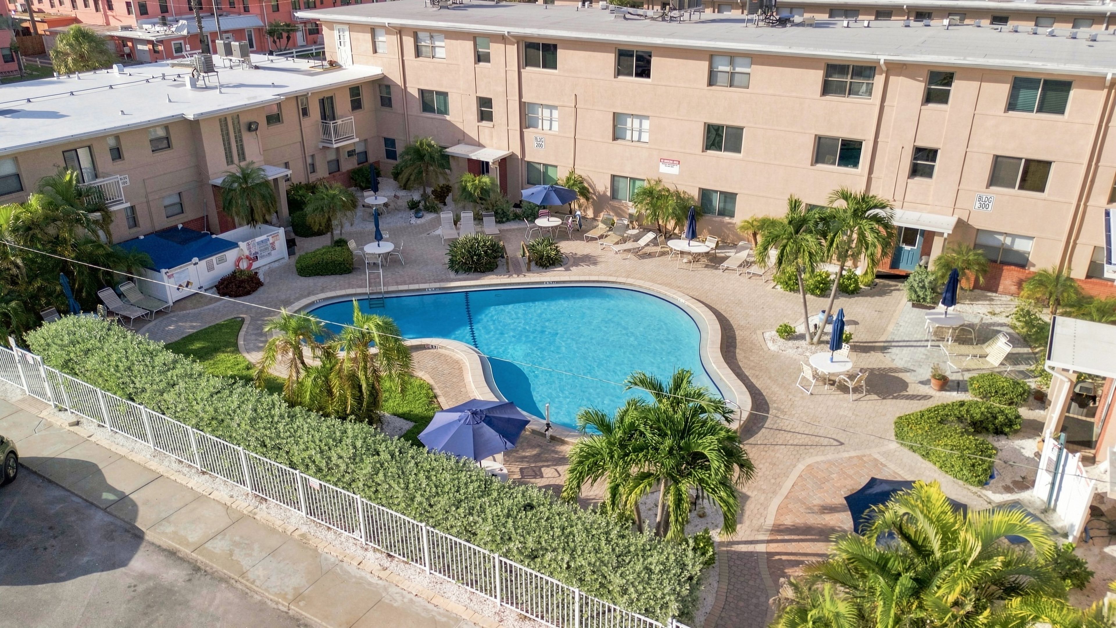 Aerial perspective of the property showcasing the central swimming pool, lush landscaping, sun loungers, and guest buildings arranged around the courtyard.