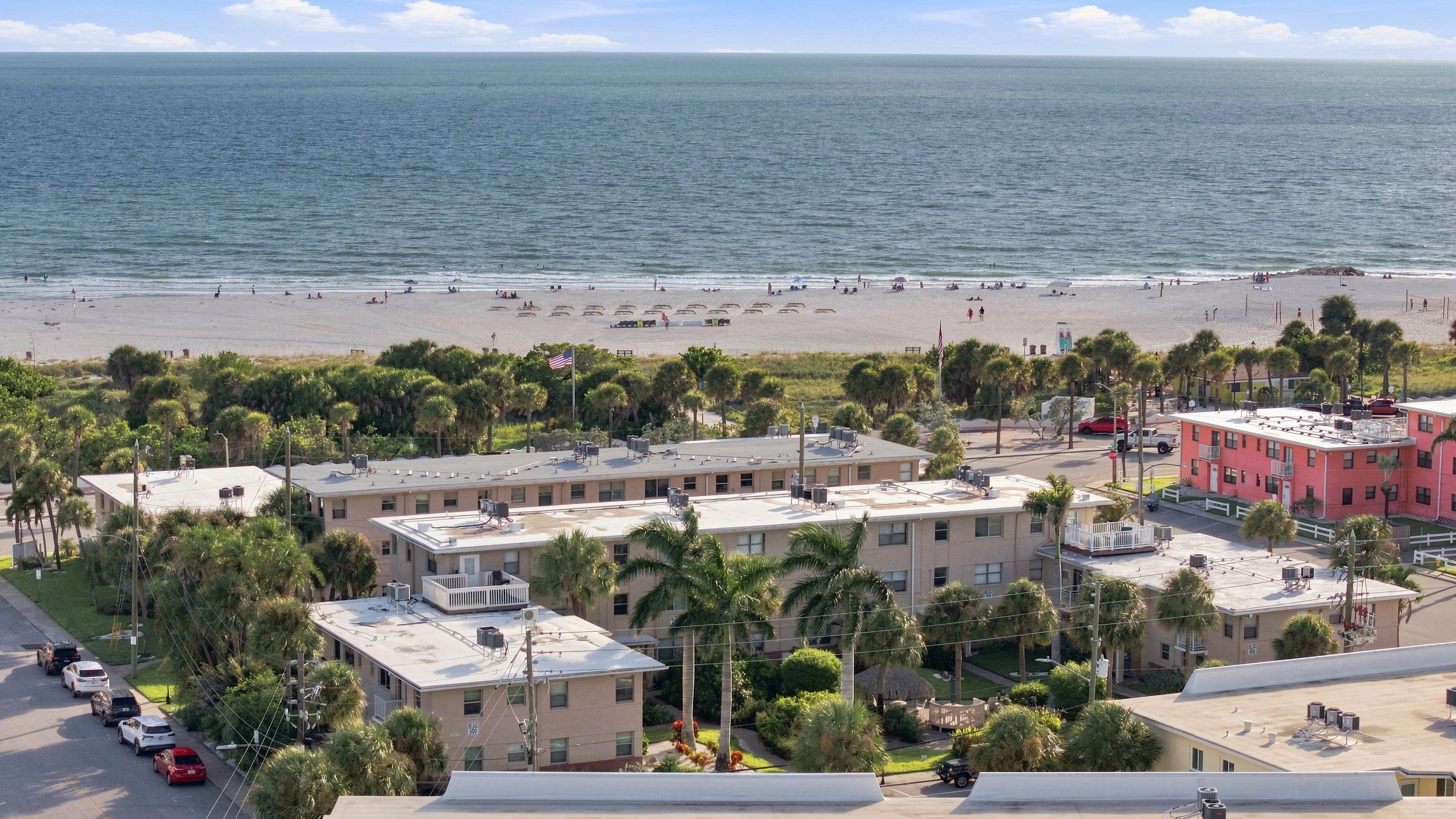 A coastal building with a flat roof, surrounded by palm trees and a beach in the background.