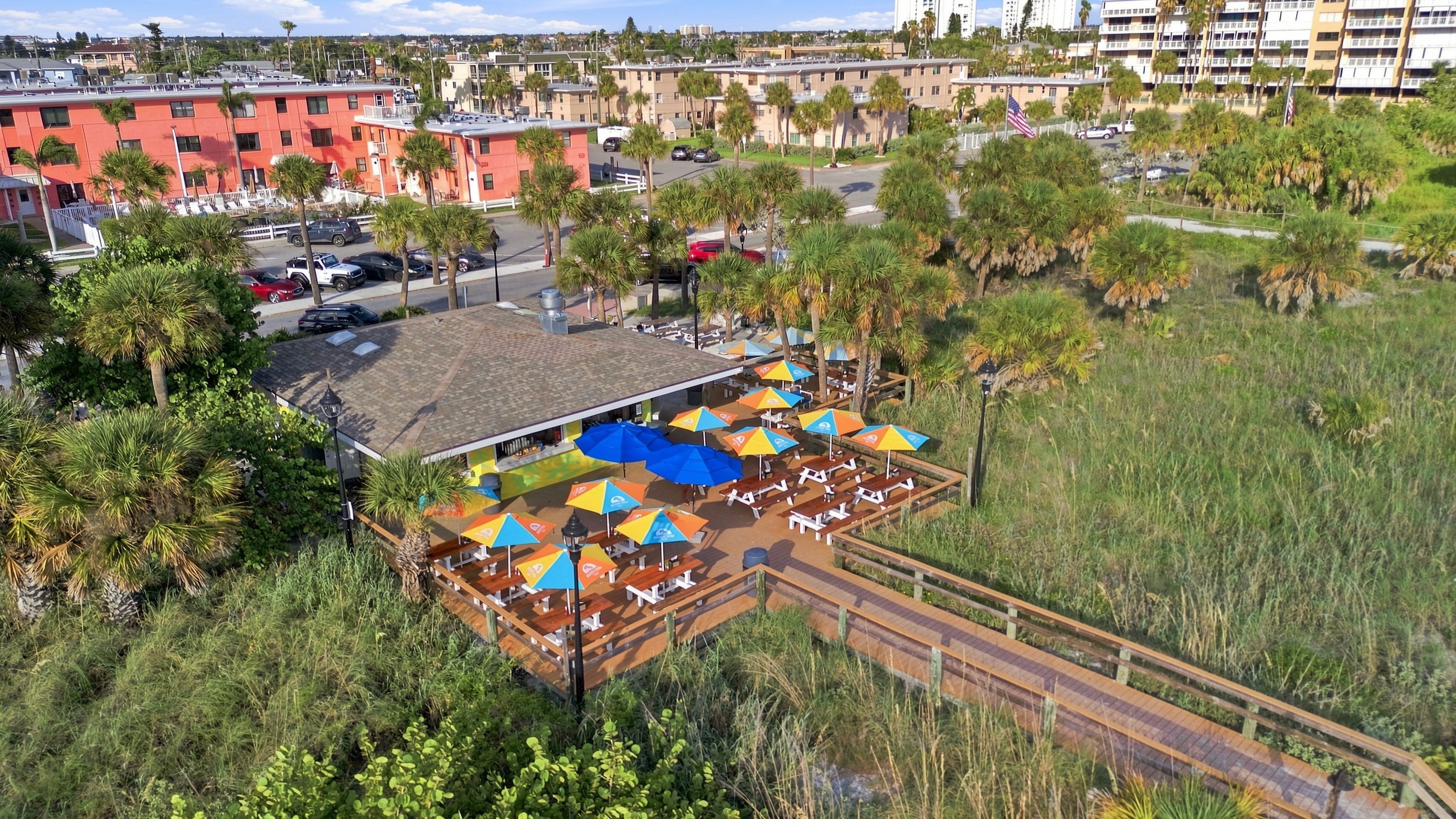 An outdoor seating area with umbrellas and tables, surrounded by palm trees and a view of a cityscape.