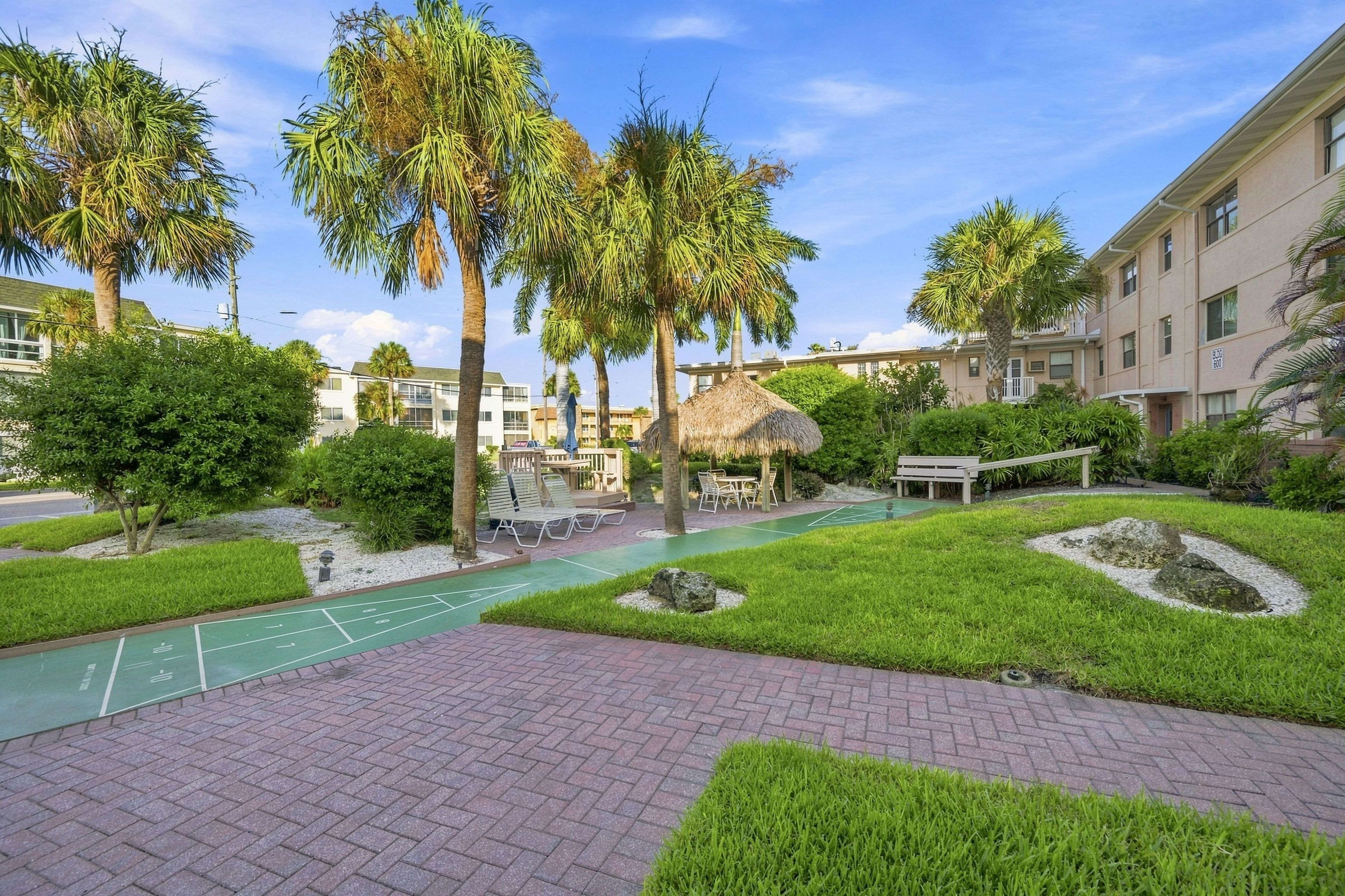 A courtyard with a shuffleboard court, palm trees, and a thatched-roof gazebo.