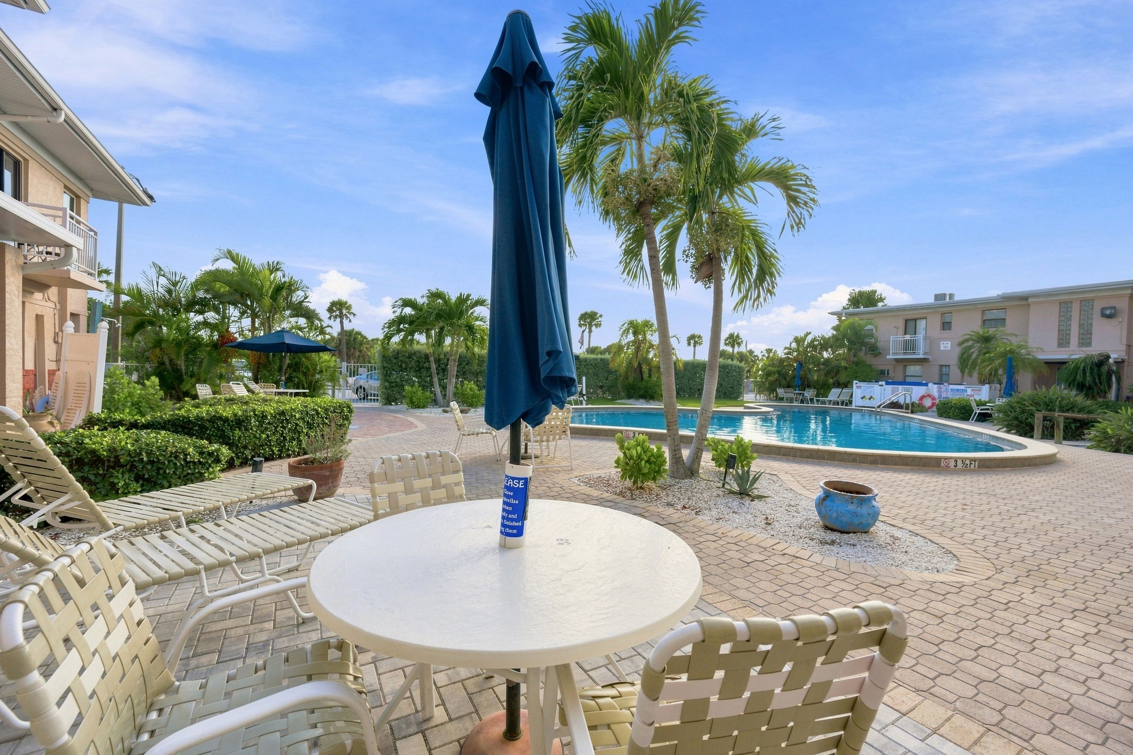 A poolside area with a table and chairs, a covered umbrella, and a pool.