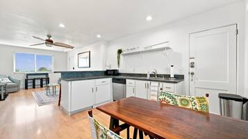 A modern kitchen with white cabinets, a wooden dining table, and a ceiling fan.