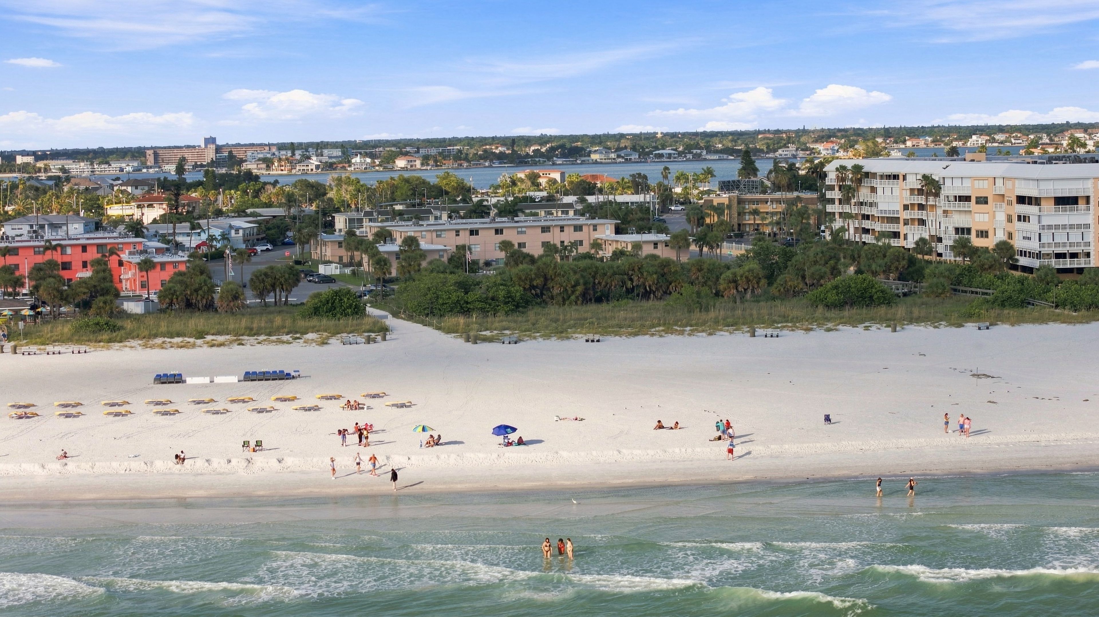 Aerial view of a coastal neighborhood with sandy beaches, lush greenery, and waterfront residential areas stretching across the horizon.