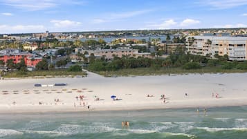 Aerial view of a coastal neighborhood with sandy beaches, lush greenery, and waterfront residential areas stretching across the horizon.