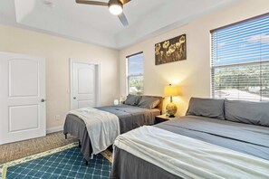 A hotel room with two beds, a ceiling fan, a window with blinds, a painting on the wall, and a lamp on the nightstand. - 4BR w/ Pool Table & BBQ just 10 Mins to the Beach (Pinellas Park)