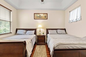 Un dormitorio con dos camas, una mesita de noche con lámpara, un cuadro en la pared y una ventana con persianas.