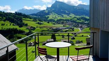 Eine Holzterrasse mit einem runden Tisch und Stühlen, mit Blick auf eine grüne Landschaft und einen Berg in der Ferne.