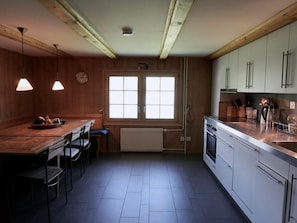 Cozinha com armários de madeira, fogão e área de refeições com cadeiras e mesa.