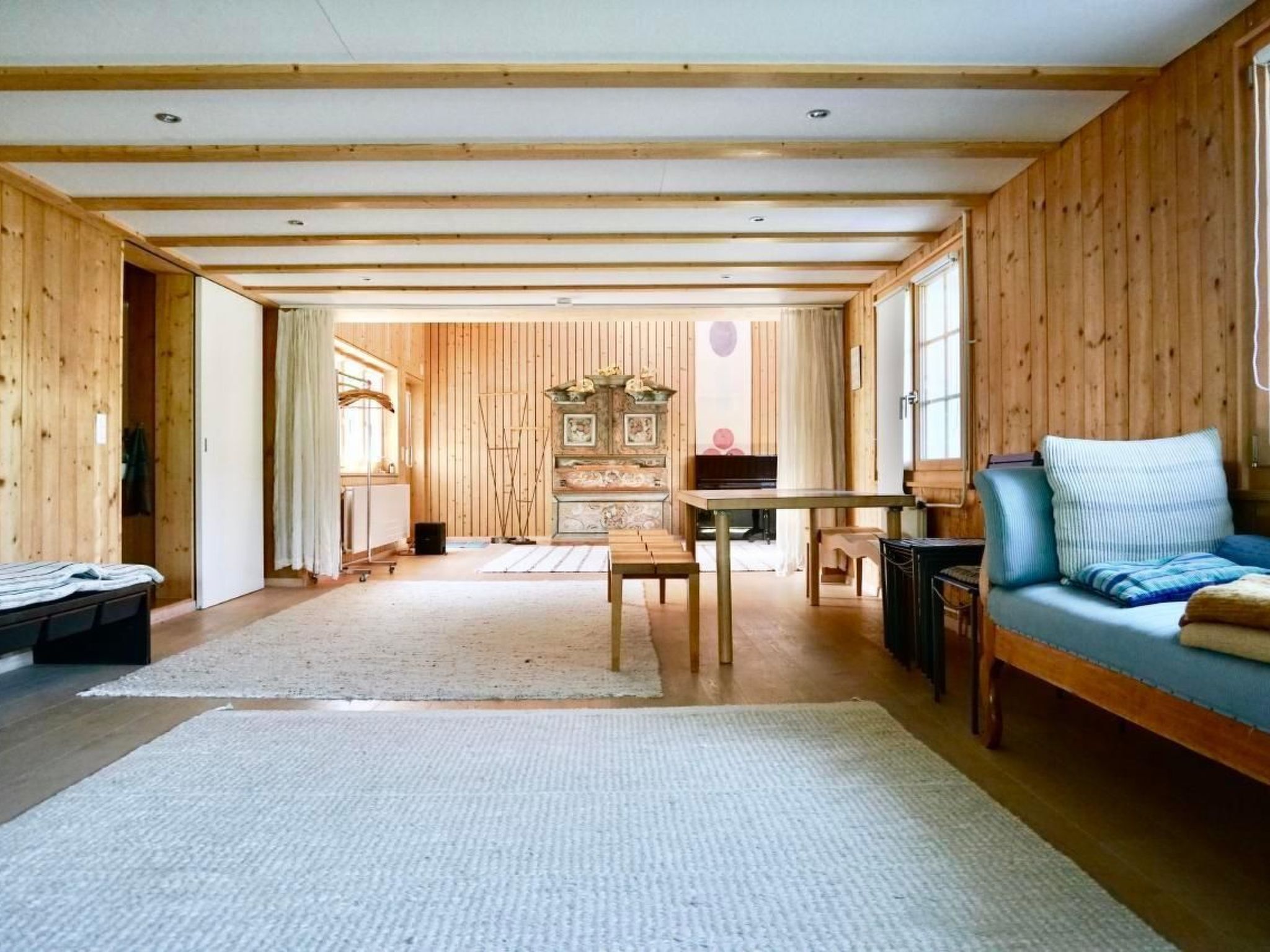 Ein geräumiger Raum mit Holzwänden und -decke, einer Couch, einem Tisch und einem Klavier.
