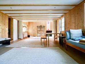 Quarto espaçoso com paredes e teto de madeira, um sofá, uma mesa e um piano.