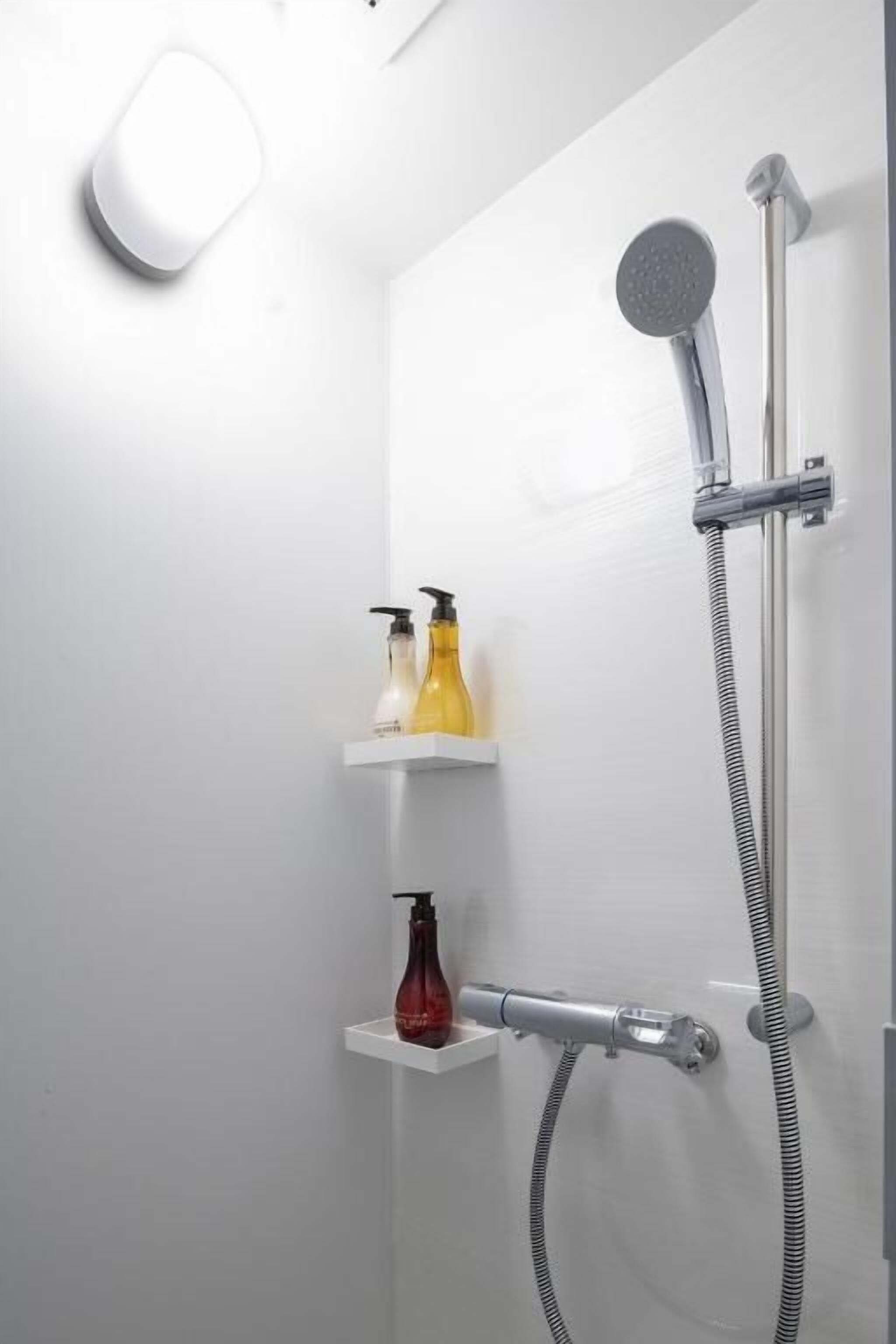 A shower with a handheld showerhead and a wall-mounted faucet, with two shelves holding toiletries.