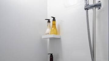 A shower with a handheld showerhead and a wall-mounted faucet, with two shelves holding toiletries.