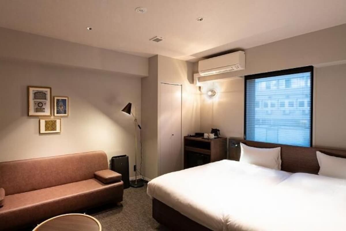 A hotel room with a bed, a sofa, a desk, and a window.
