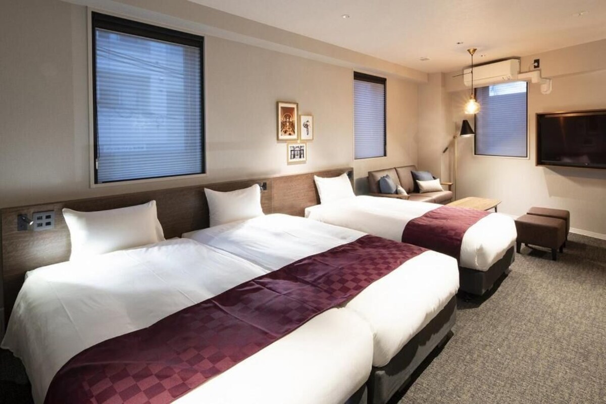 A hotel room with two beds, a flat-screen TV, a desk, and a lamp.