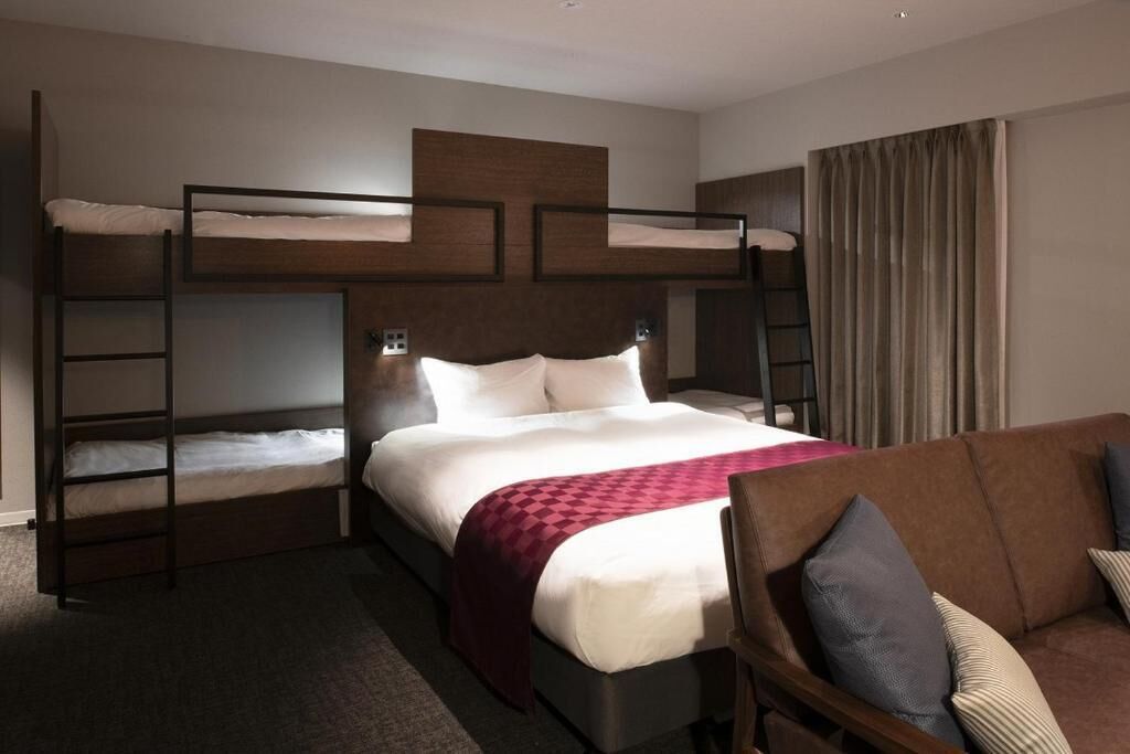 A hotel room with a bunk bed, a sofa, and a bedside table.
