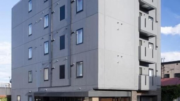 A multi-story building with a flat facade, rectangular windows, and a visible entrance with a ramp. - ALPHABED INN Otaru Ekimae (Otaru)