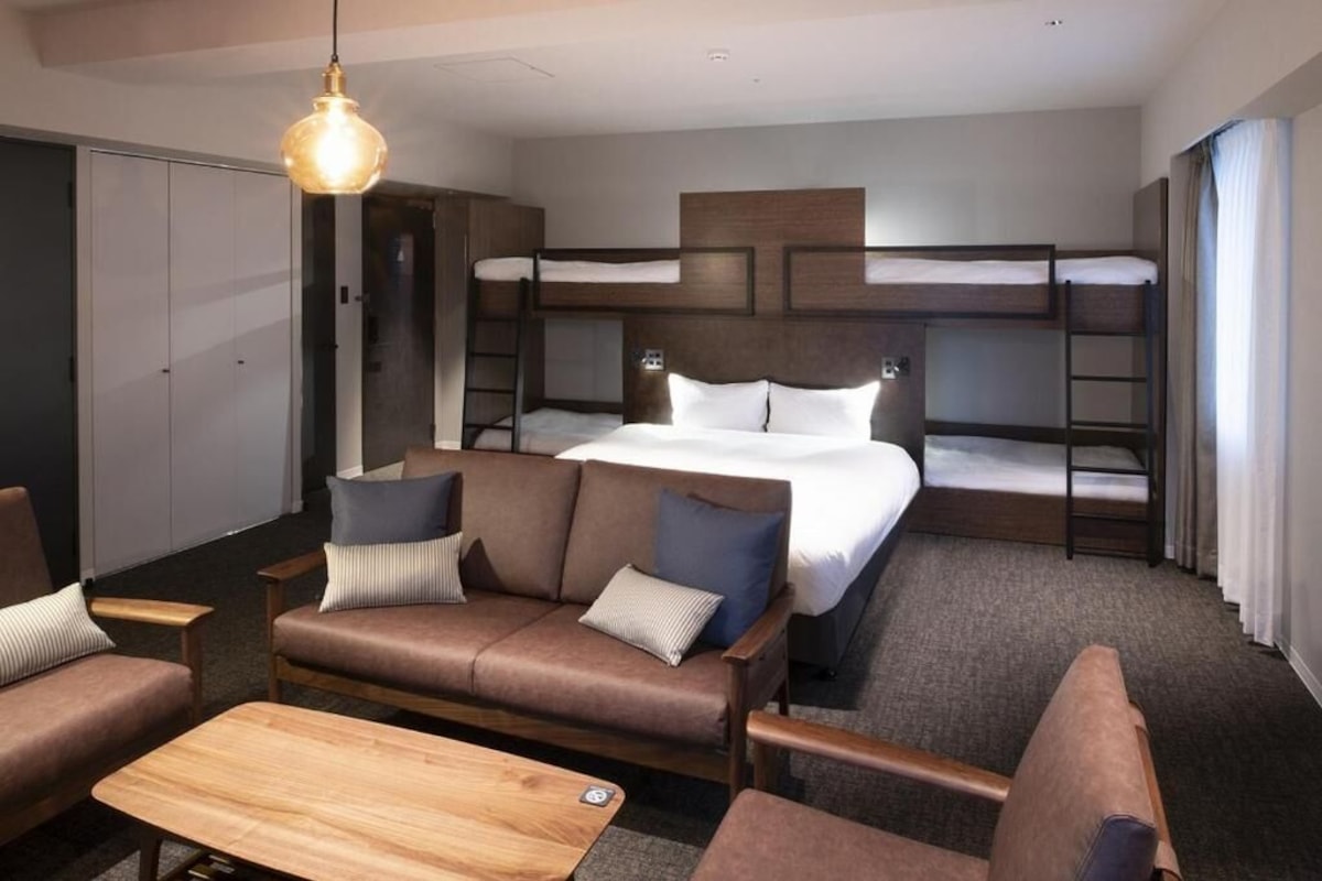 A hotel room with bunk beds, a sofa, a coffee table, and a hanging light fixture.