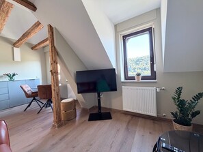Ein modernes Wohnzimmer mit Flachbildfernseher, Holzbalken, einem Essbereich und einem Fenster mit Blick.