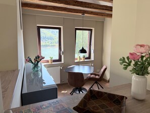 Eine moderne Küche mit einer zentralen Kochinsel, zwei Fenstern mit Blick ins Grüne und einem Essbereich mit Tisch und Stühlen.