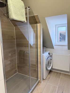 Ein modernes Badezimmer mit Duschkabine aus Glas, einer integrierten Waschmaschine und einem Fenster für natürliches Licht.