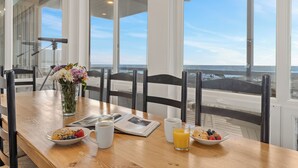Mesa de café da manhã com vista para o oceano, um vaso de flores e um jornal.