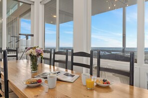 Une table de petit-déjeuner avec vue sur l’océan, un vase de fleurs et un journal.