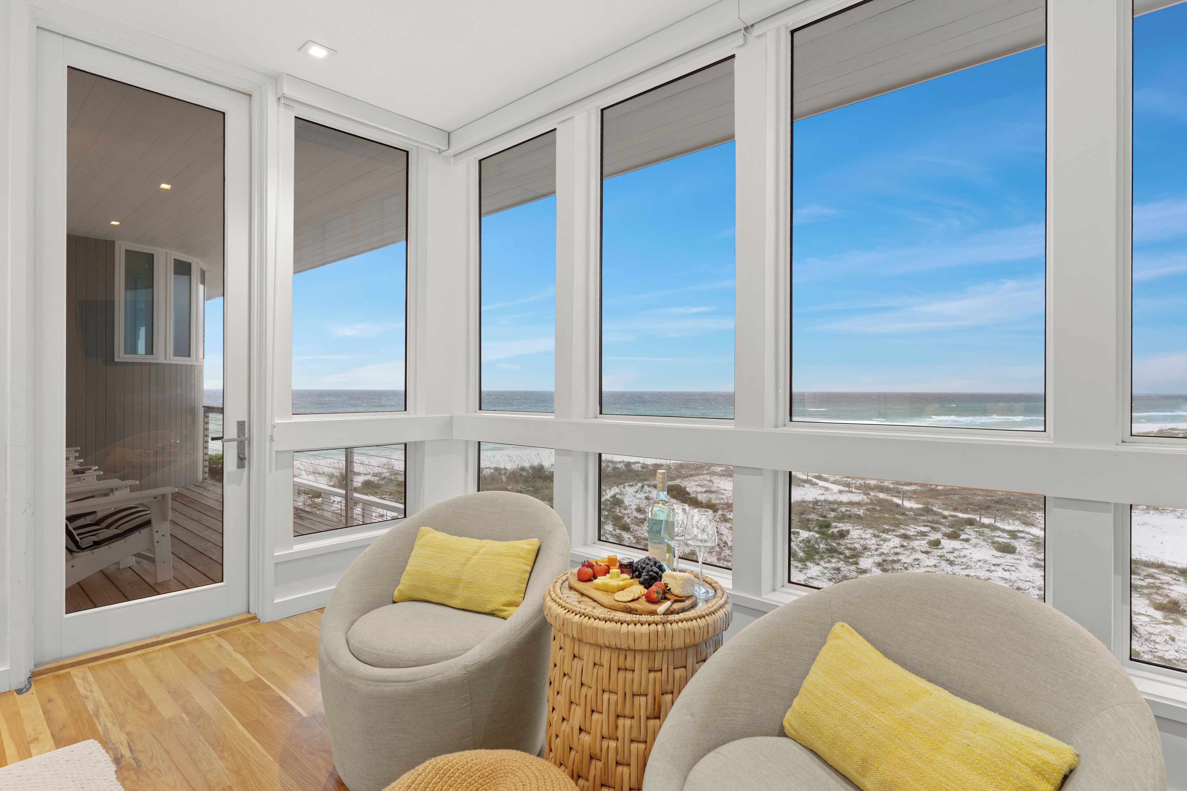 A room with large windows overlooking a beach, furnished with two chairs and a small table with snacks.