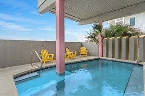 Une piscine avec une terrasse en béton, une colonne rose et des chaises Adirondack jaunes.