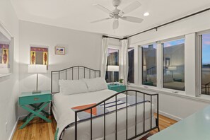 Une chambre à coucher avec un lit, une table de chevet, une fenêtre et un ventilateur de plafond.